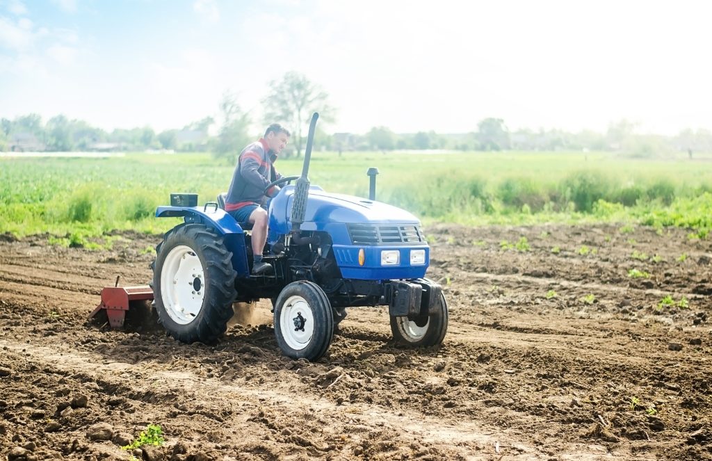 A farmer on a tractor works on the field. Growing crops in a small agricultural family enterprise. Small business support. Farming and agriculture. Cultivation technology equipment. Food production