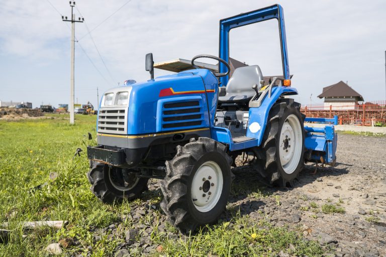 A small mini blue tractor stands on a farm yard on green grass and waits for work to begin