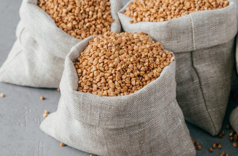 Eco food and clean eating concept. Buckwheat in small linen bags. Wooden spoon filled with protein product, Copy space on grey background.