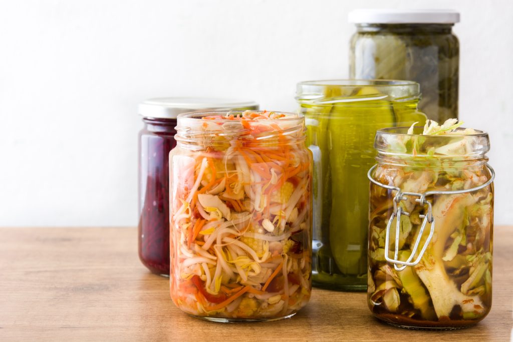 Fermented preserved vegetables in jar on wooden table.