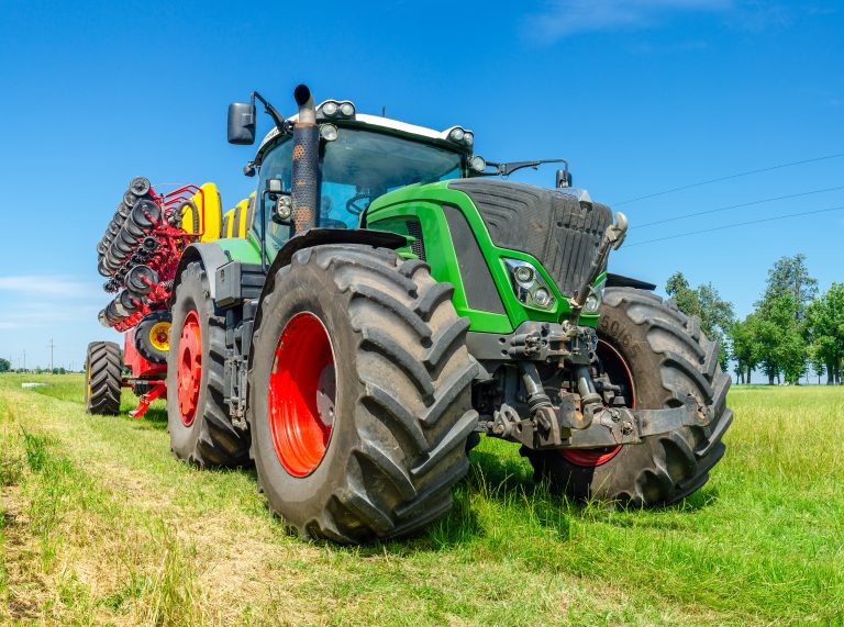 New big red modern farm tractor with quad tracks for powerful combine with renewable energy food and power crisis parked sunshine farmers rural agricultural field with wind turbine electric generator.