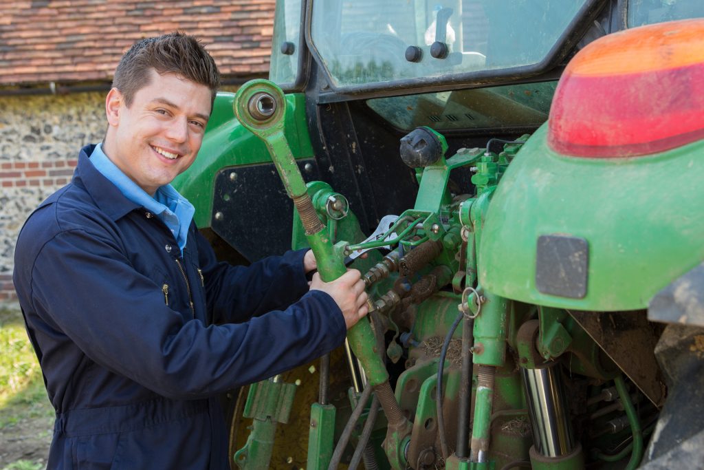 Portrait Of Mechanic Repairing Tractor On Farm