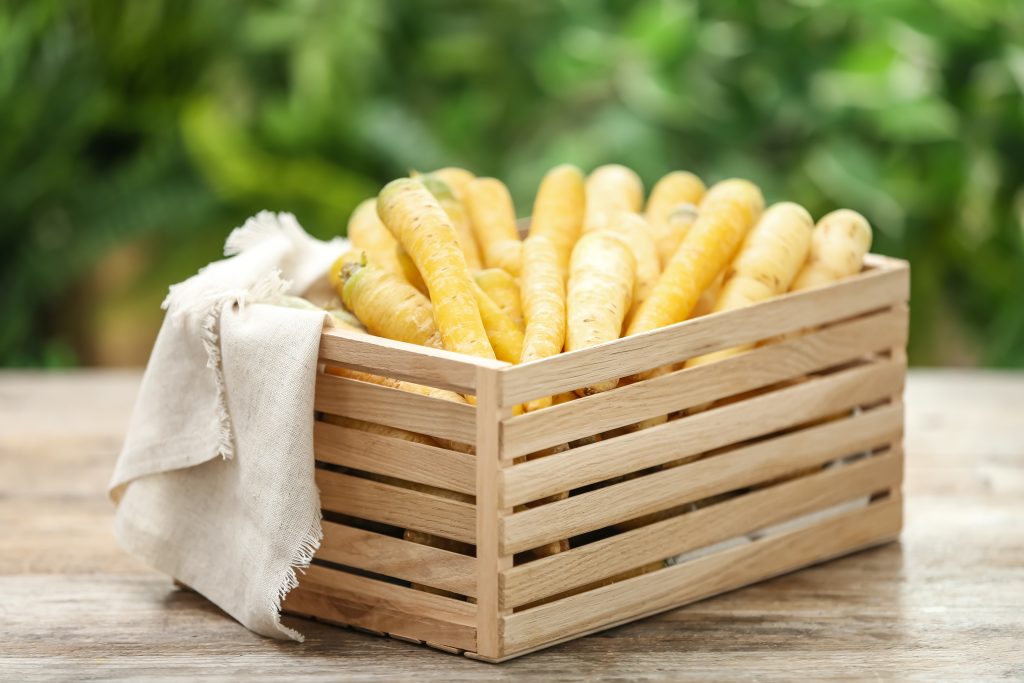 Raw white and yellow carrots in crate on wooden table against blurred background