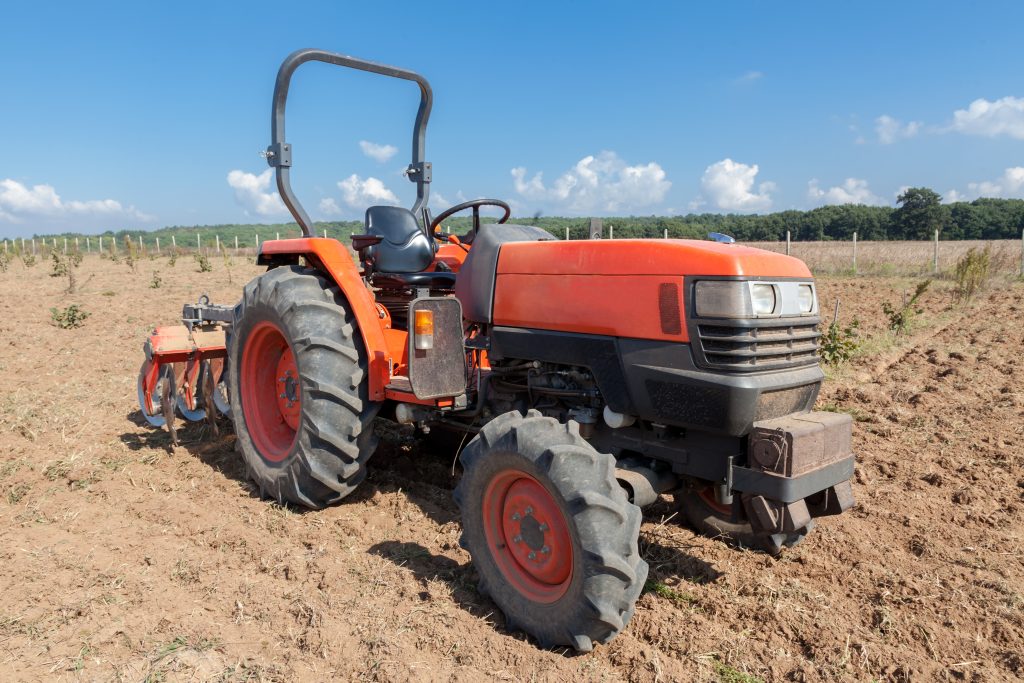 Small red tractor with plow in field.