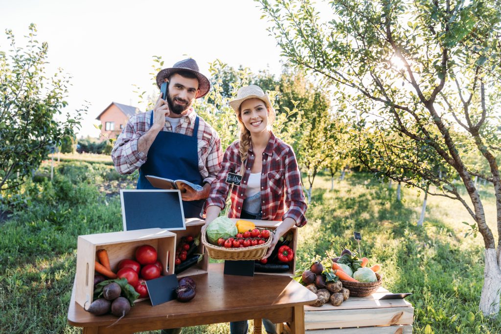 two smiling farmers selling organic locally grown vegetables at market