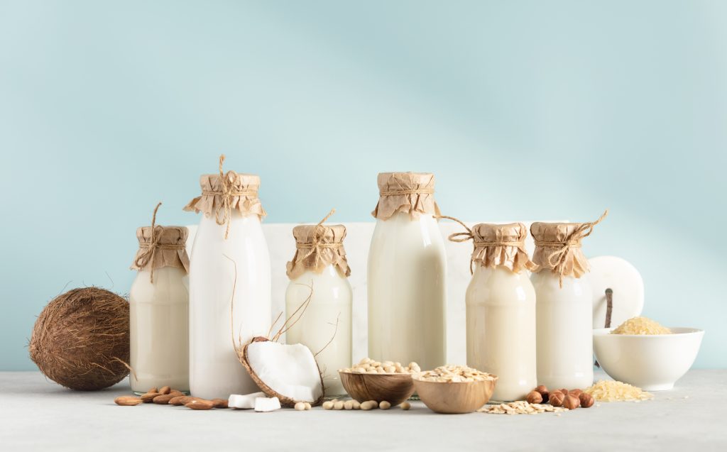 Vegan non dairy plant based milk in bottles and ingredients on blue background. Alternative lactose free milk substitute