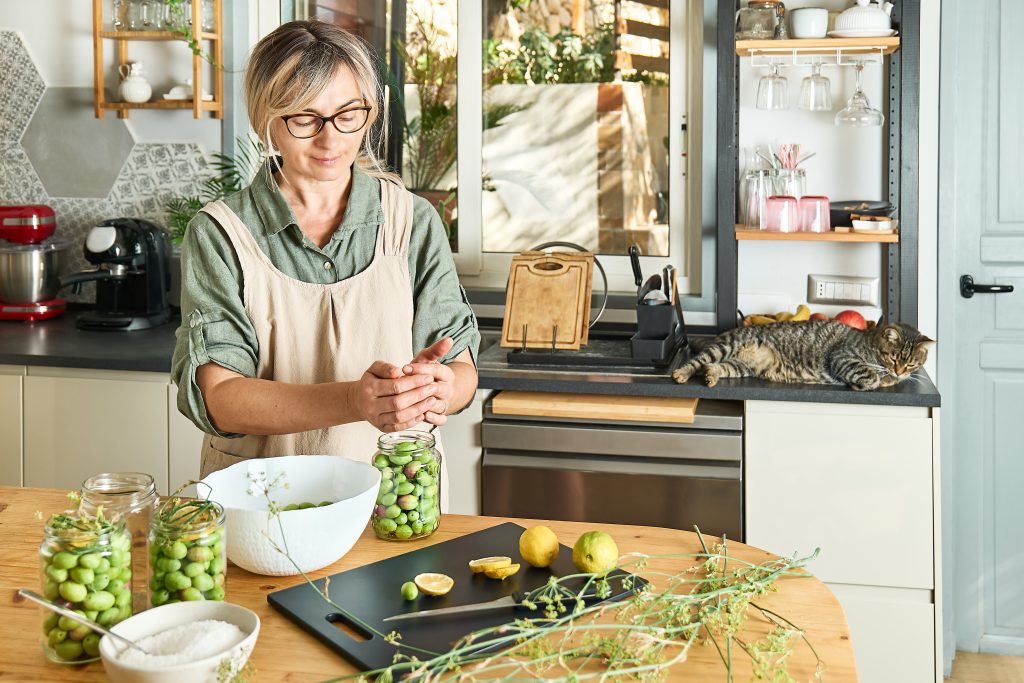 Woman preparing fermented olives in glass jar with slices of lemon, wild fennel and canning brine. Autumn vegetables canning. Healthy homemade food. Conservation of harvest.