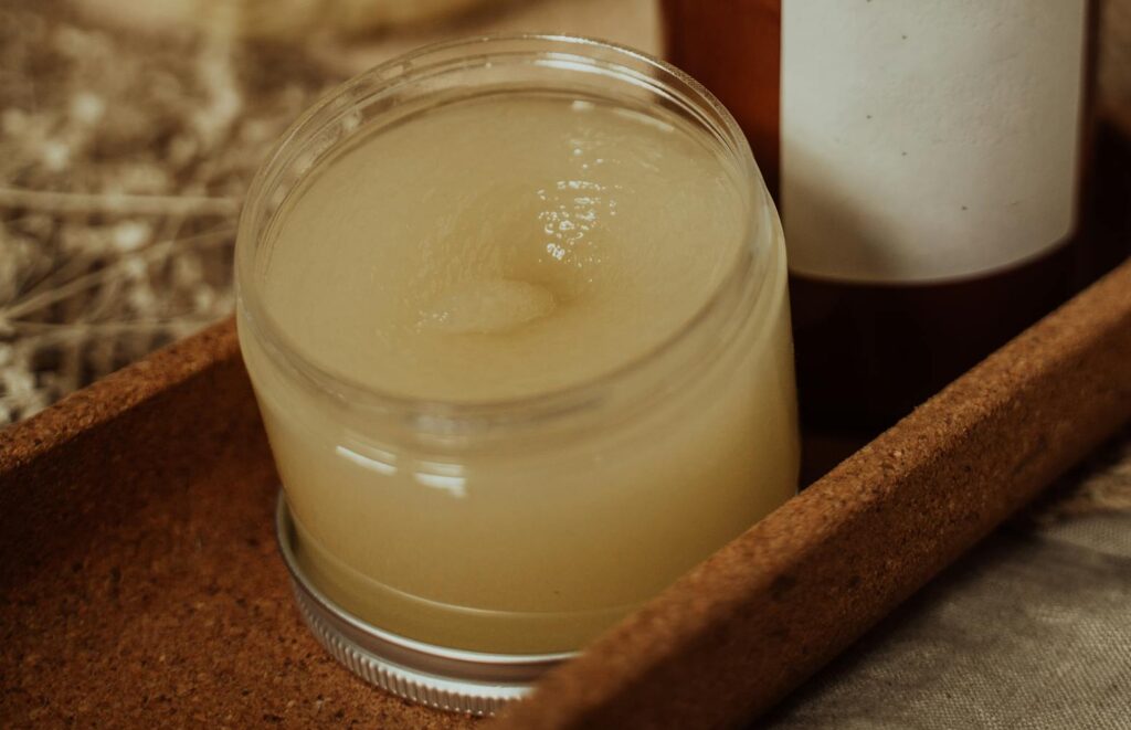 Cozy setup featuring a handmade beeswax candle and cosmetic balm jar on textured fabric.