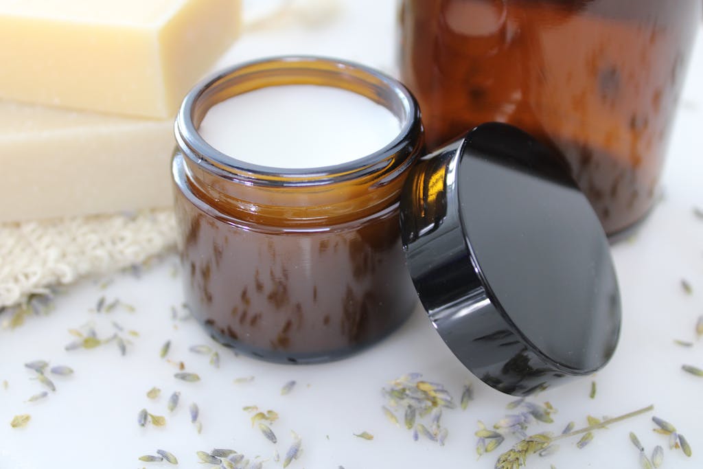 Delicate natural cream in amber glass jar, surrounded by lavender and beeswax, perfect for skincare routines.