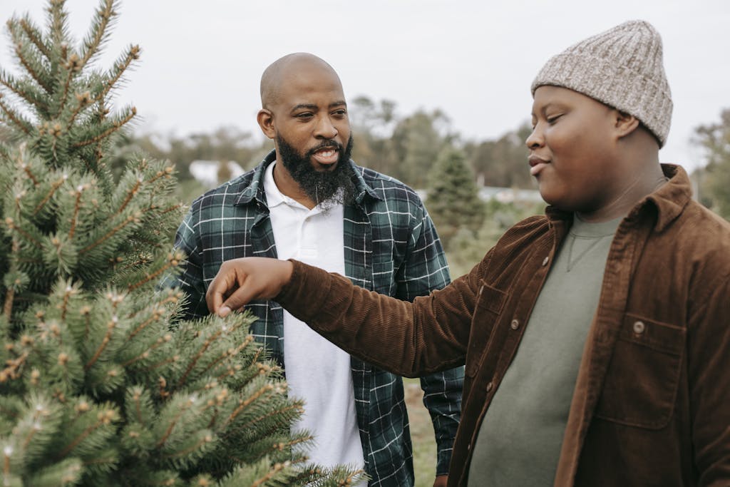 Father and son picking a Christmas tree together at a tree farm, enjoying a holiday outing.