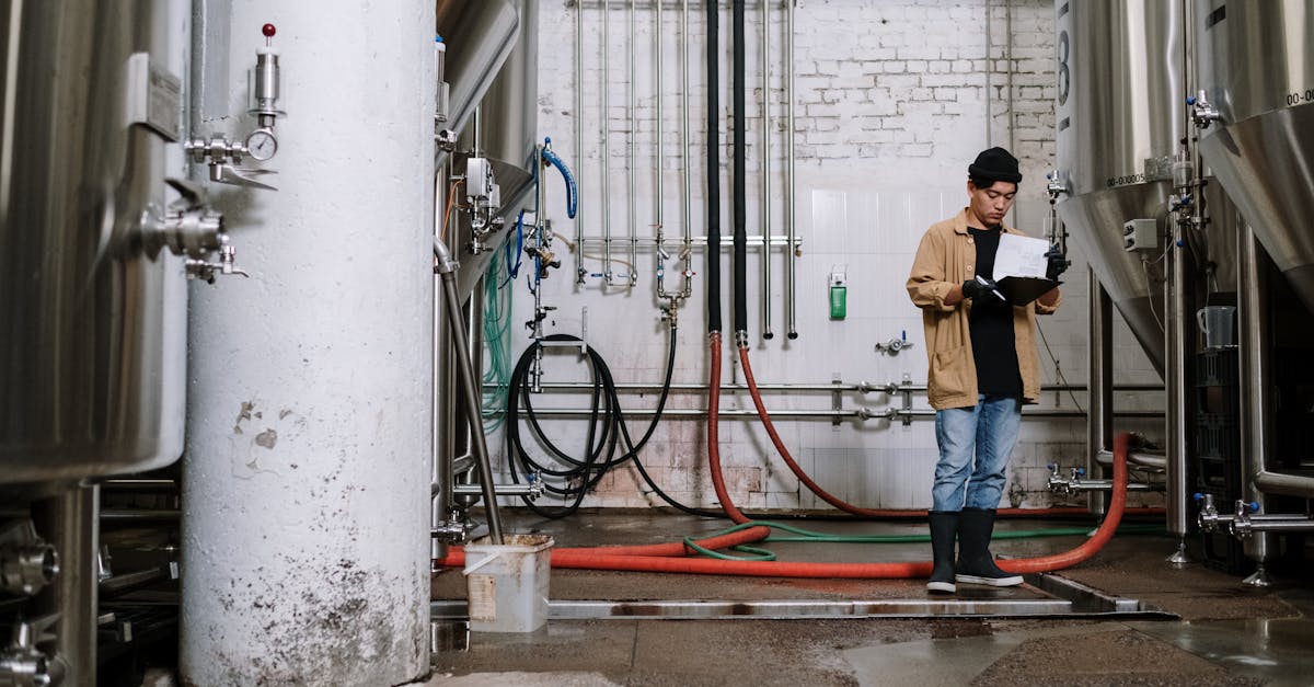 a brewery worker inspects equipment in a brewing facility surrounded by fermentation tanks