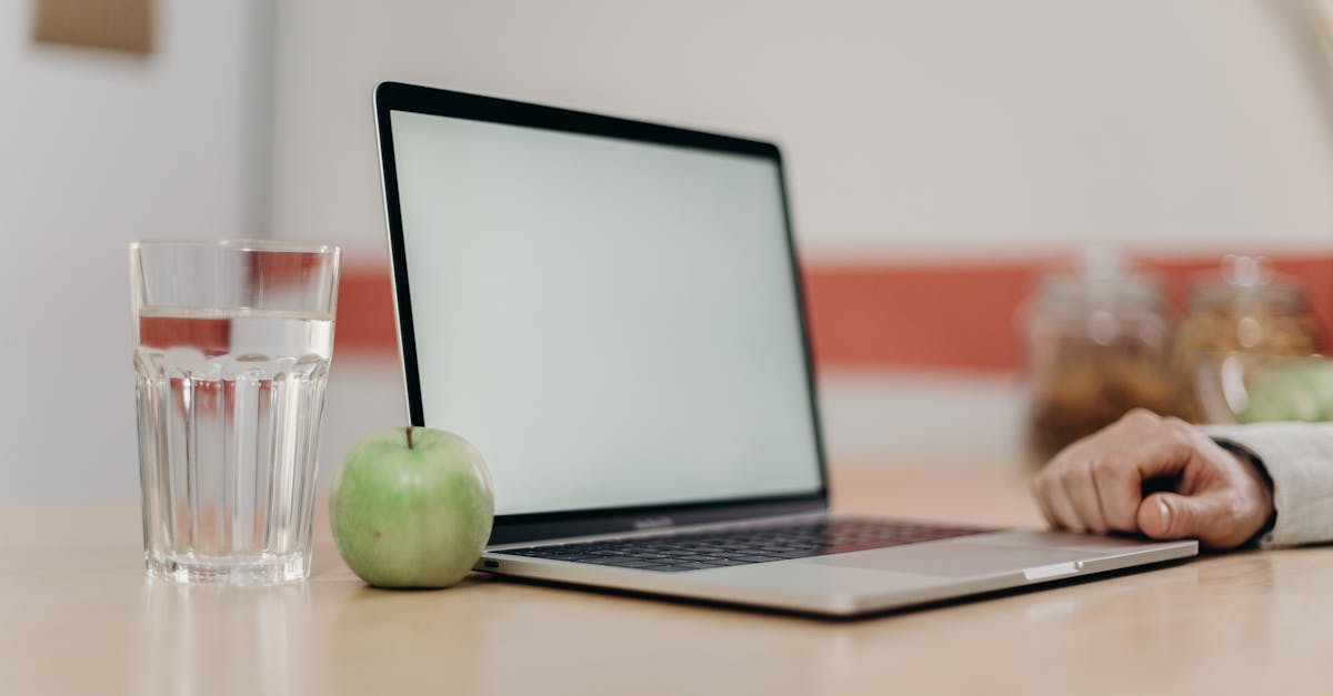 a clean and minimal home workspace with a laptop green apple and a glass of water on a desk