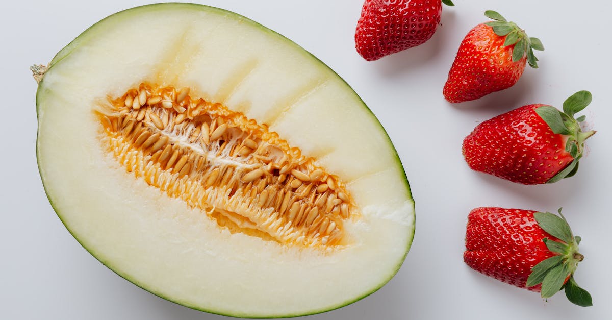 a close up of a halved melon and fresh strawberries on a white background