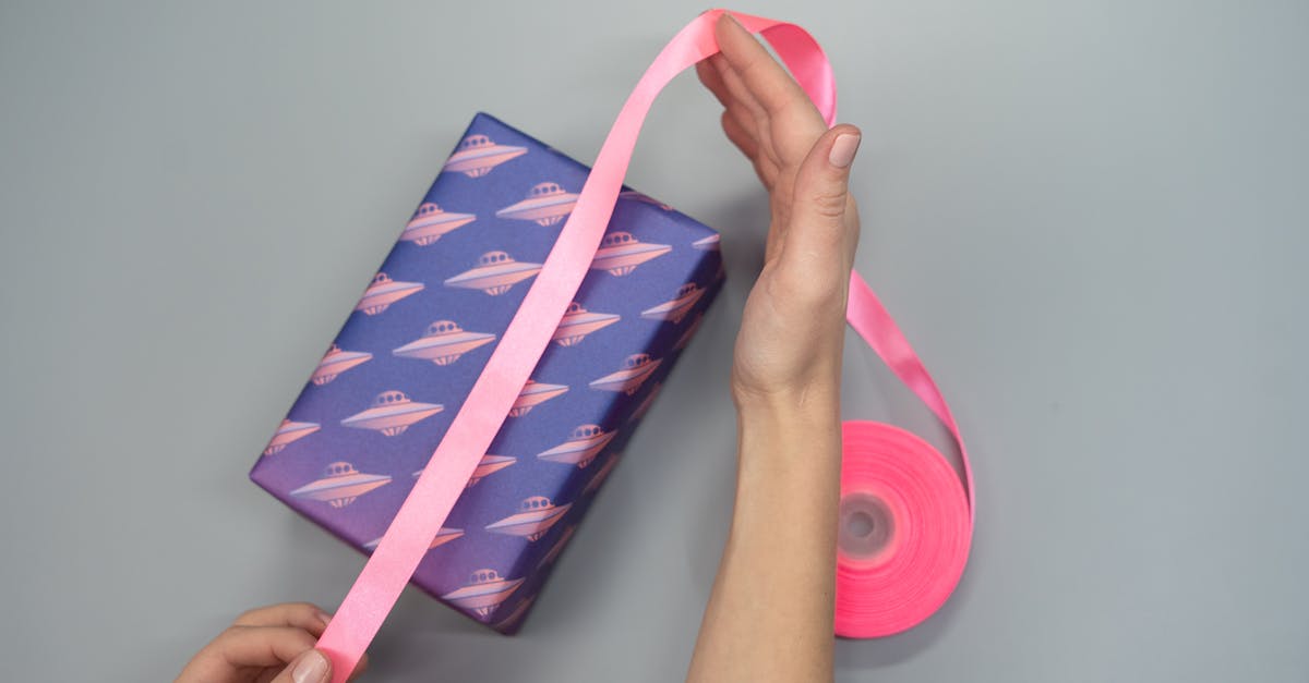 a close up of hands wrapping a gift box with pink ribbon and ufo themed paper