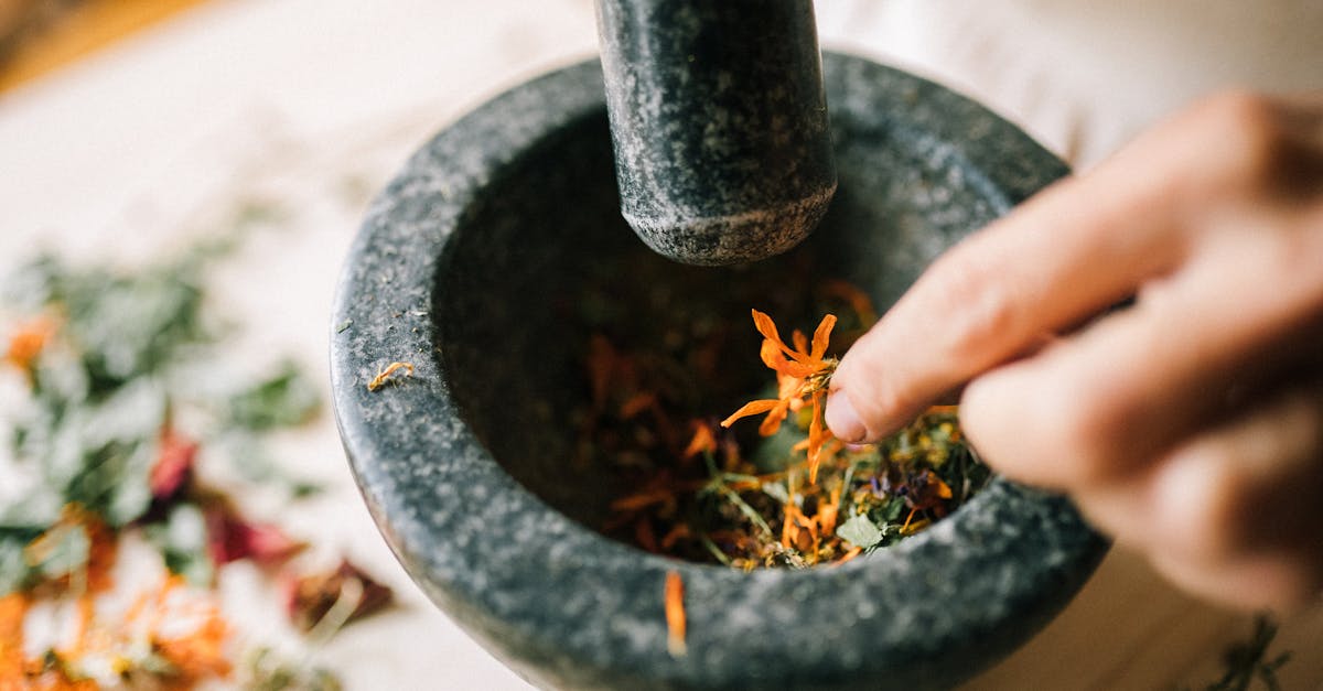 a hand crushes vibrant herbs in a stone mortar blending natural ingredients