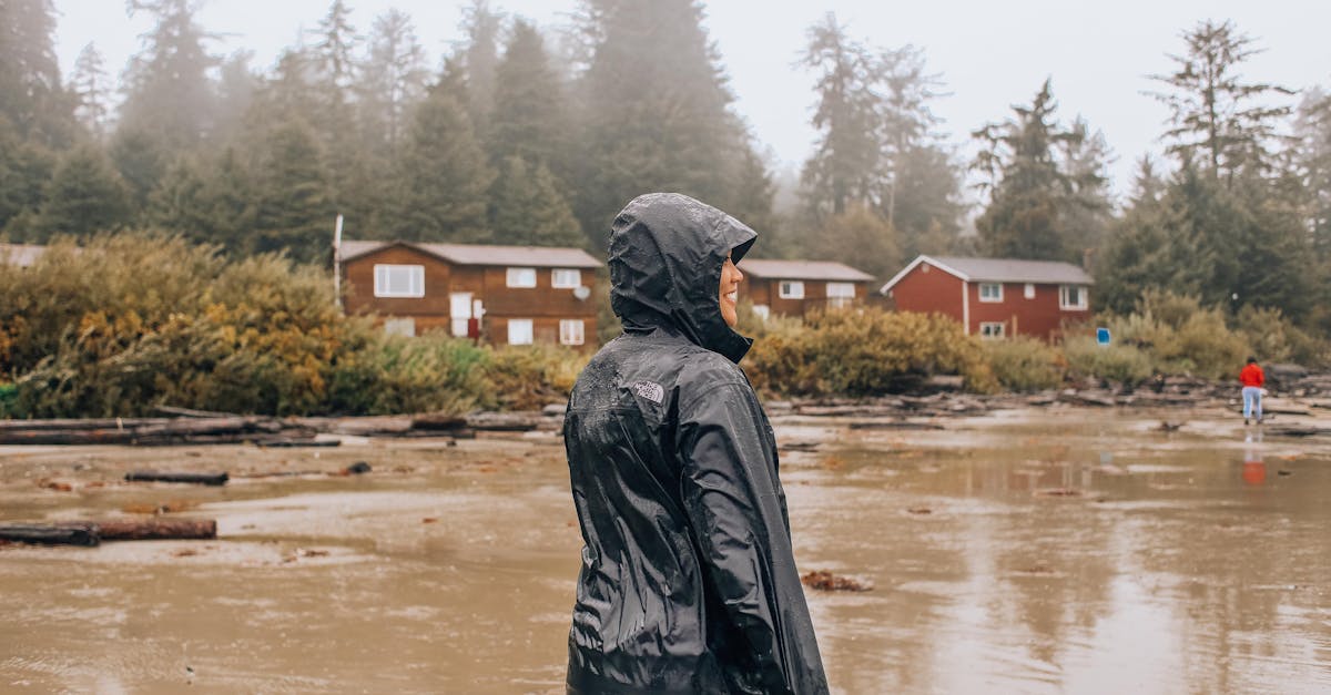 a person in rain gear stands on a rainy day near wooden cabins surrounded by trees