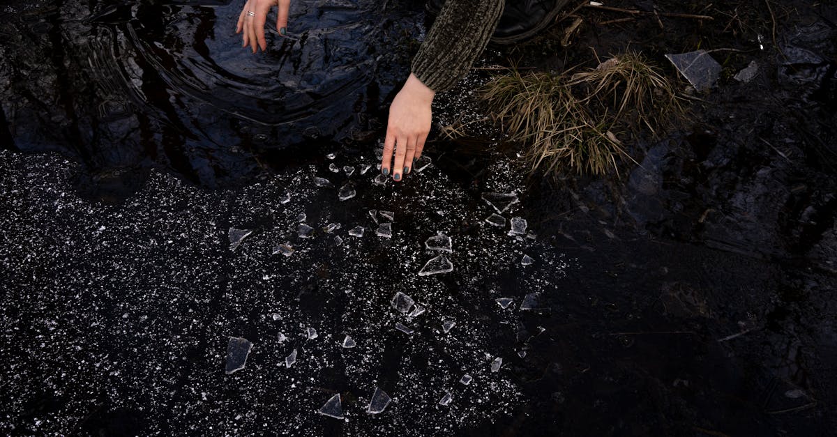 a person with a green sweater breaks thin ice on a dark pond surface