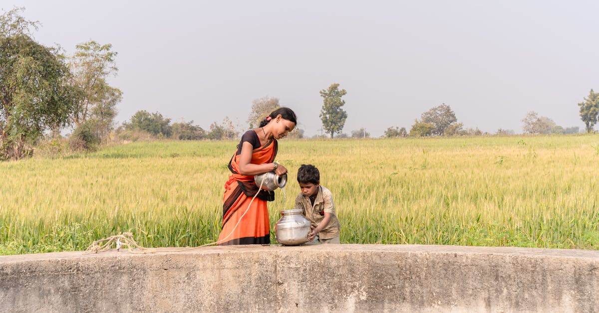 a rural scene with a woman and child gathering water by a lush field