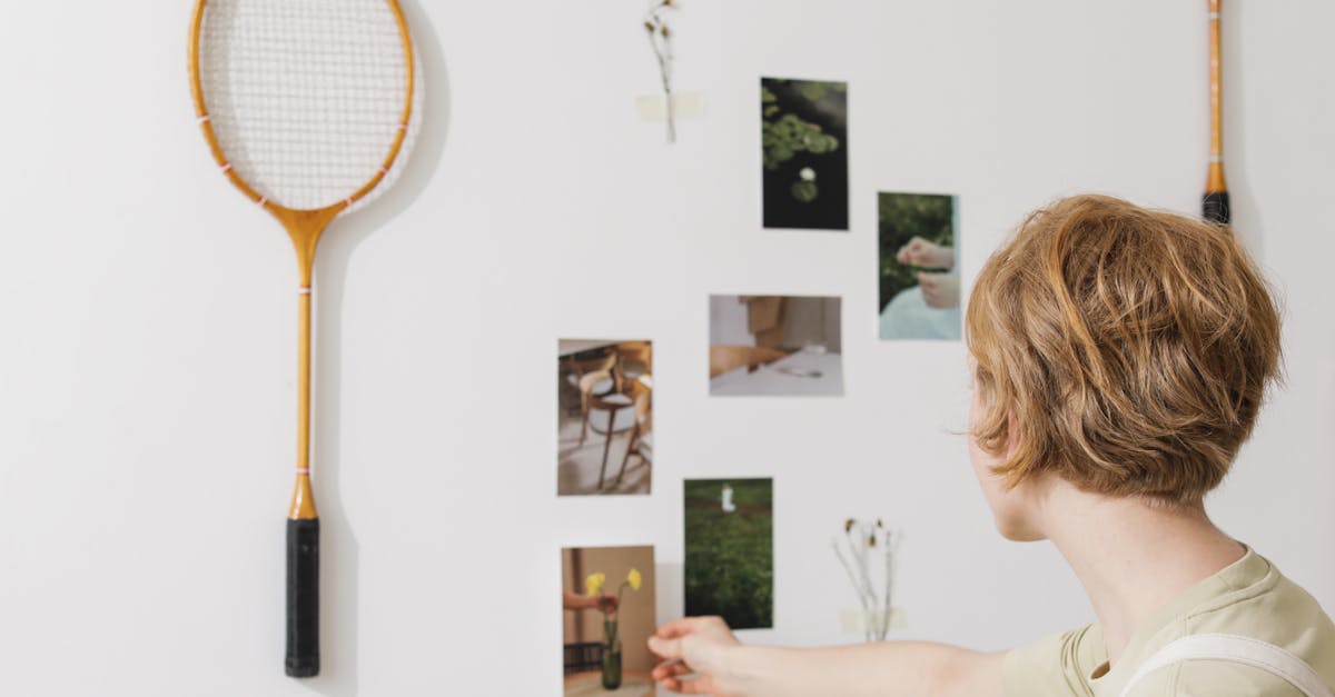 a woman arranges photos and tennis rackets on a wall sparking creativity and inspiration