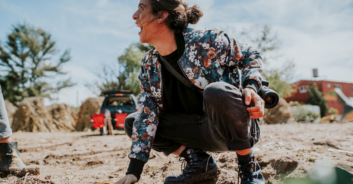 a woman crouching in a sunlit rural field wearing a floral jacket and boots