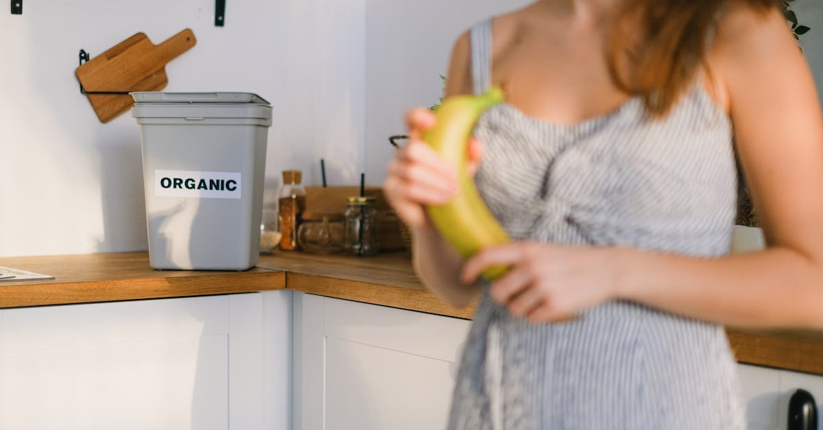 a woman in a kitchen holding a banana with an organic bin in view