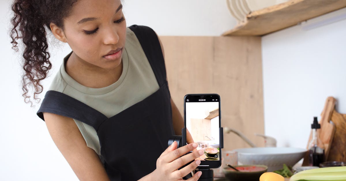 a young woman filming a cooking tutorial in her kitchen using a smartphone