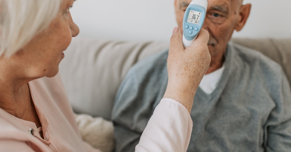 an elderly woman checks the temperature of a senior man using a digital thermometer indoors