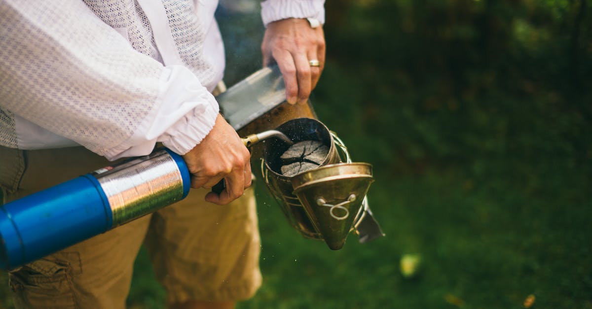 close up of a beekeeper operating a smoker outdoors illustrating traditional beekeeping practices