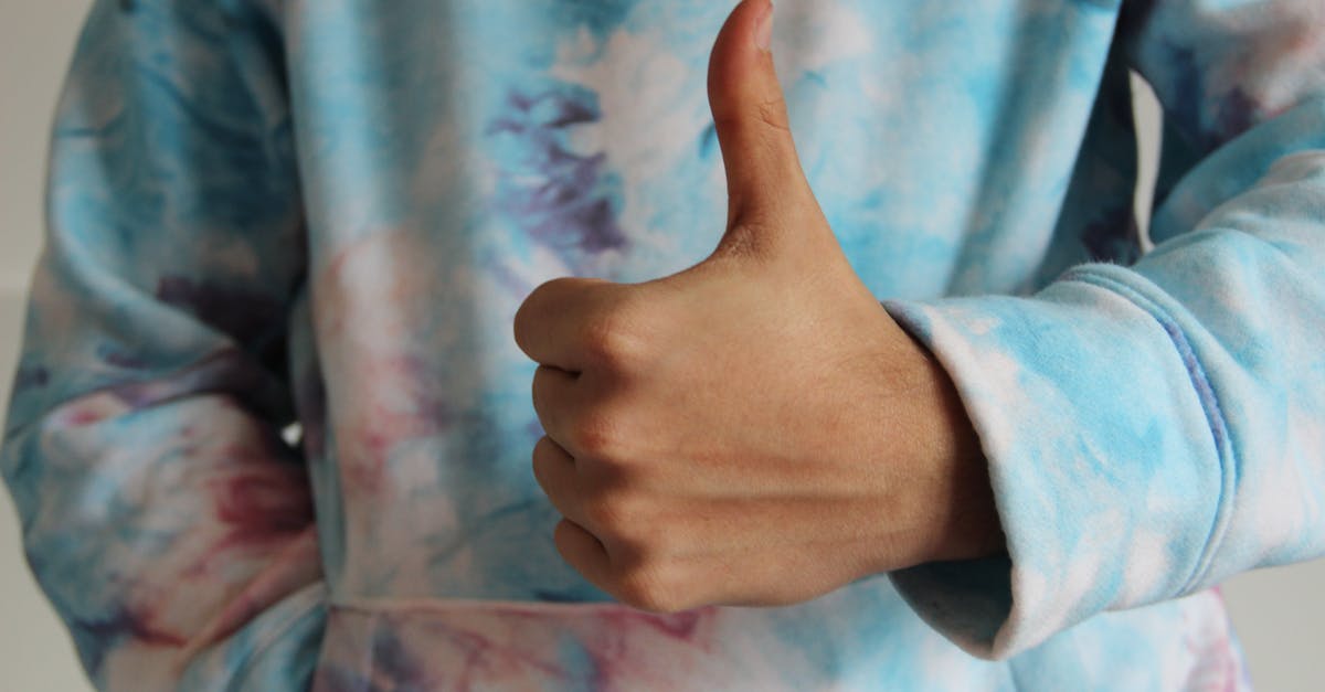 close up of a hand giving a thumbs up sign while wearing a colorful tie dye hoodie