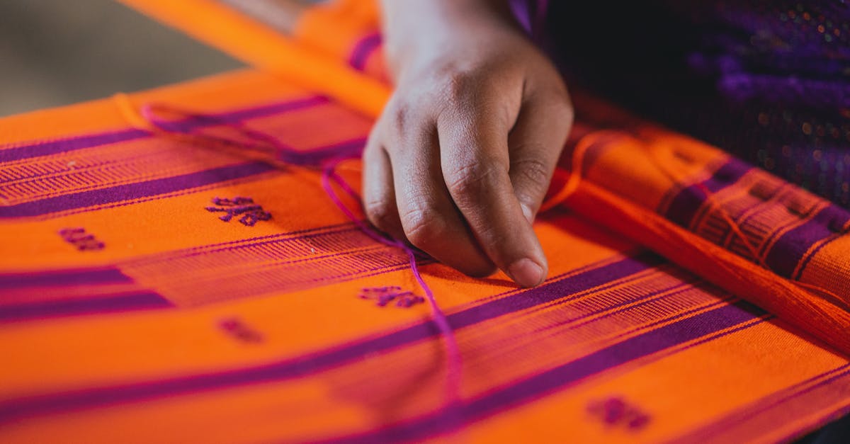 close up of a hand weaving a vibrant orange and purple textile showcasing traditional craftsmanship