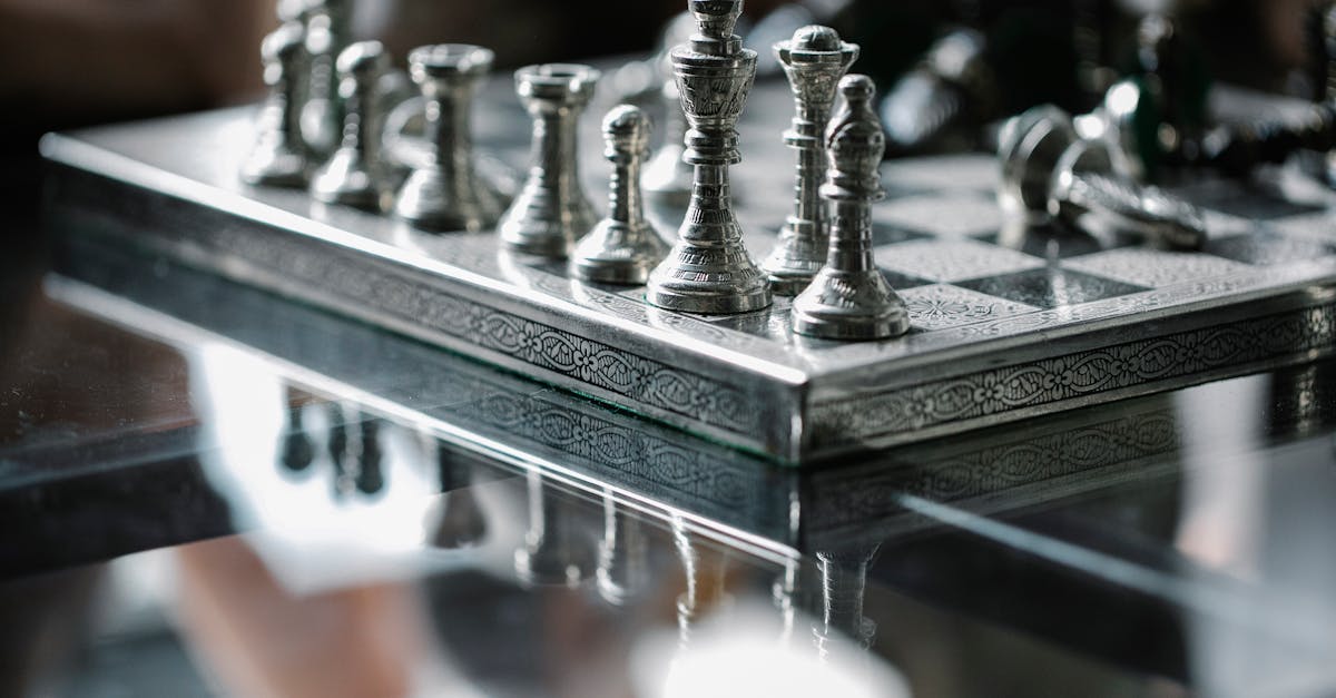 close up of a metallic chess set on a reflective glass table emphasizing strategy and design