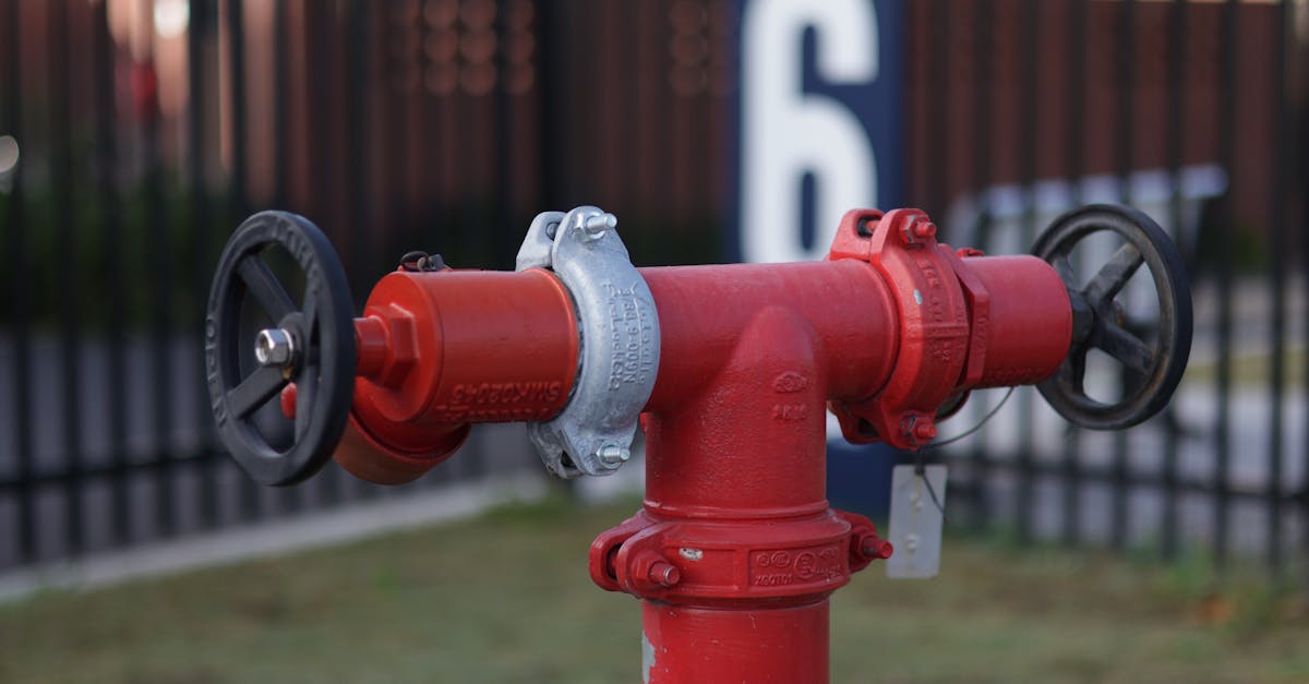 close up of a red industrial valve hydrant in an outdoor setting with a fence backdrop