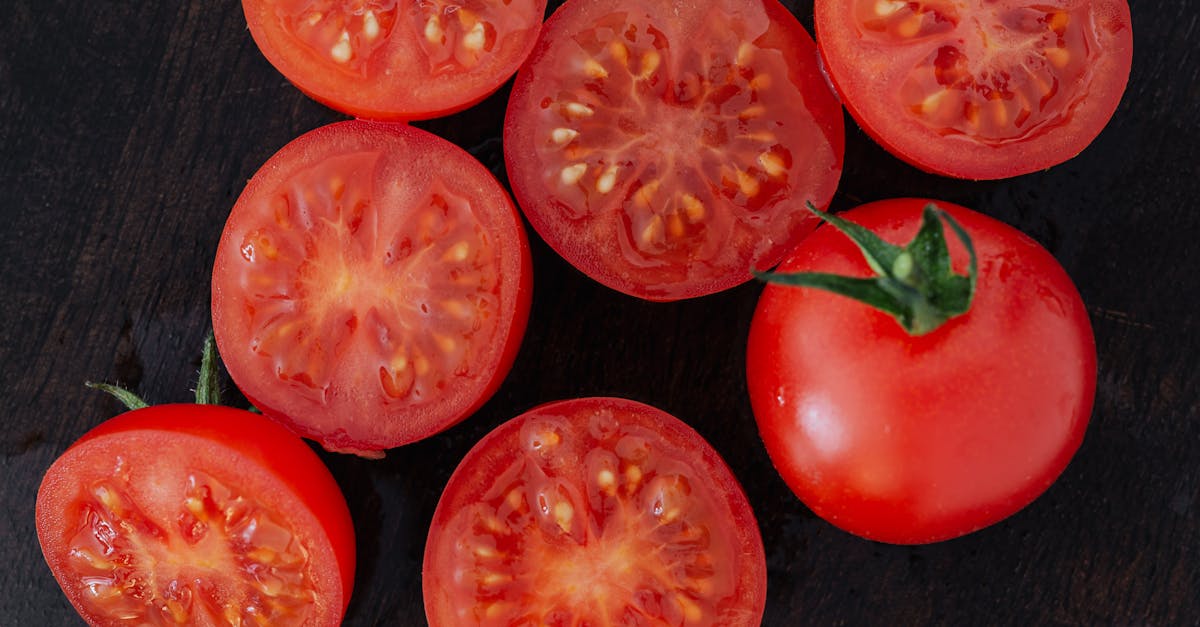 close up of fresh ripe tomatoes and slices on a dark wooden surface showcasing their vibrant red co