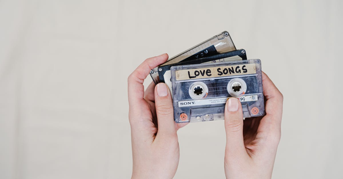 close up of hands holding retro cassette tapes labeled love songs on a light background