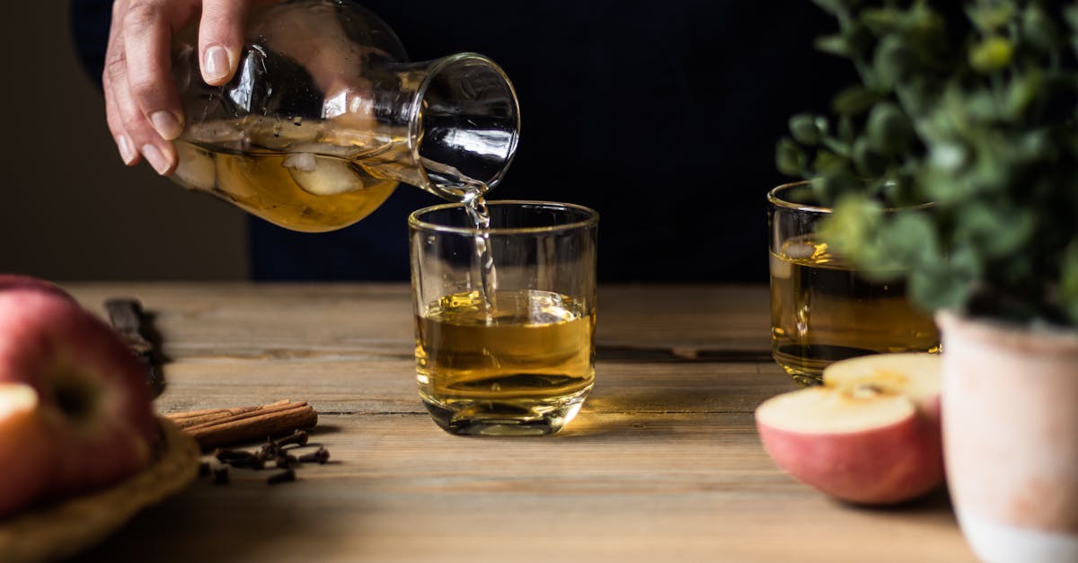 close up of someone pouring apple cider into glasses on a wooden table with apples and spices