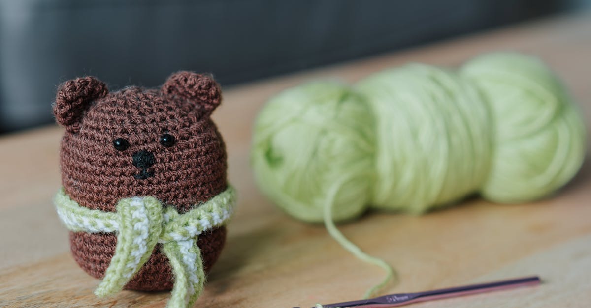 closeup of small dark brown crochet toy bear and crochet next to light green threads on wooden table