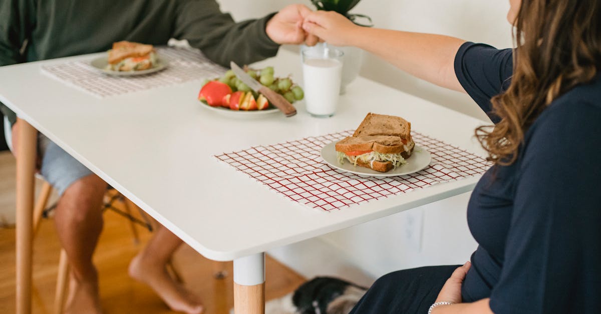 crop anonymous happy couple in casual clothes holding hands above table with sandwiches and plate wi