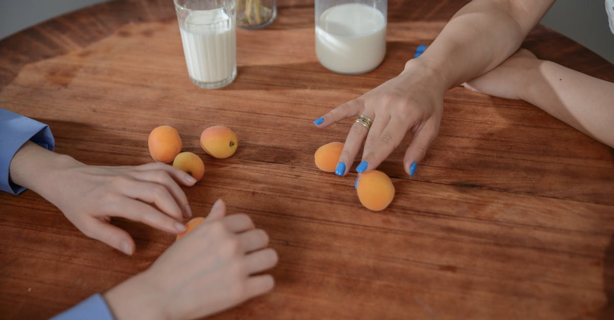 hands reaching for apricots on a wooden table with milk depicting everyday life