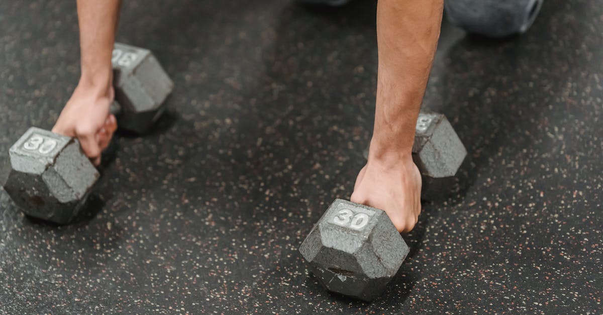 high angle of crop anonymous male athlete standing on knees with dumbbells while training on floor i 1