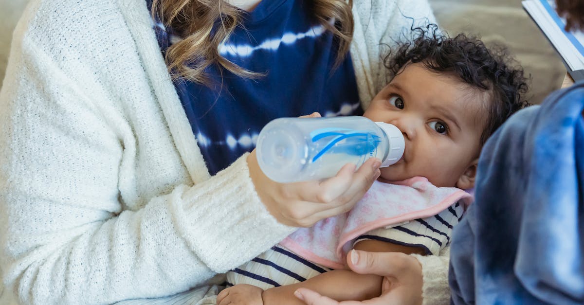 high angle of crop mother embracing little african american baby and feeding from bottle sitting on