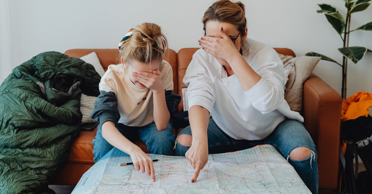 mother and daughter covering eyes while pointing at map on couch planning a trip