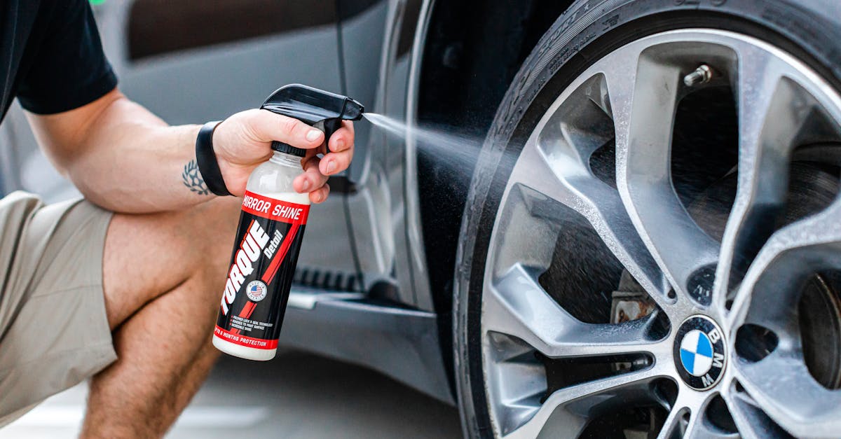 person using a spray bottle to clean the rim of a car wheel outdoors