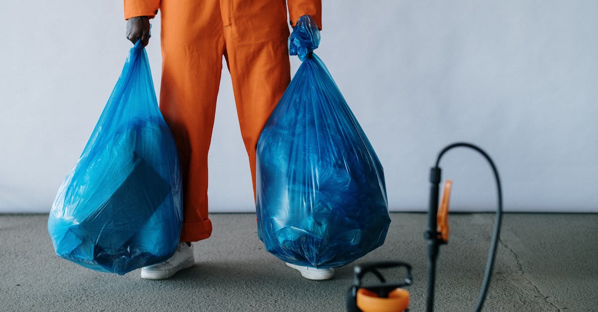 sanitation worker in orange overalls holding blue trash bags indoors for waste management