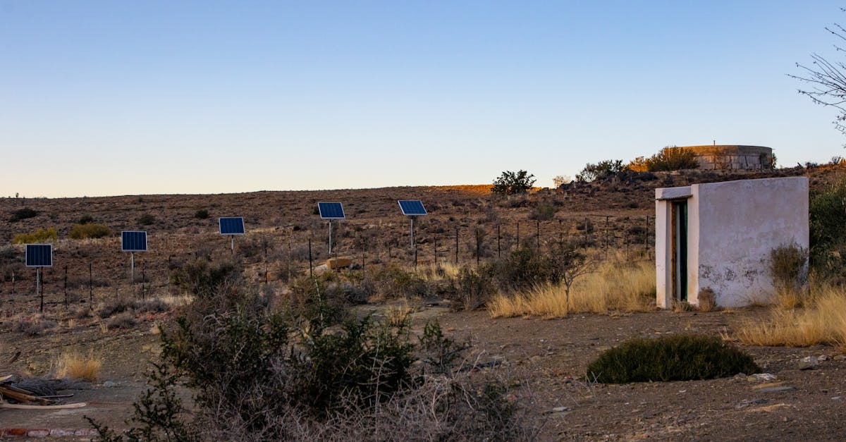 solar panels in a desert landscape with a shed under a clear sunset sky