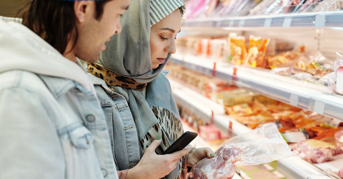 two adults shopping for meat products in a supermarket using a smartphone to compare choices