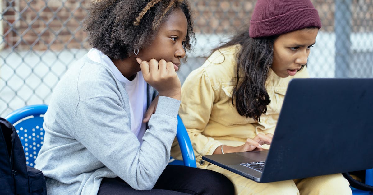 two diverse schoolgirls attentively sharing a laptop outdoors fostering learning and friendship