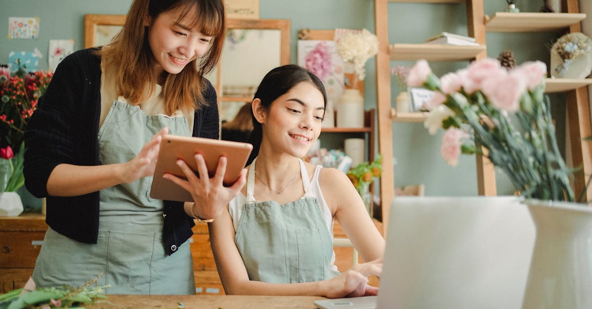 two smiling florists working together with digital devices in a flower shop