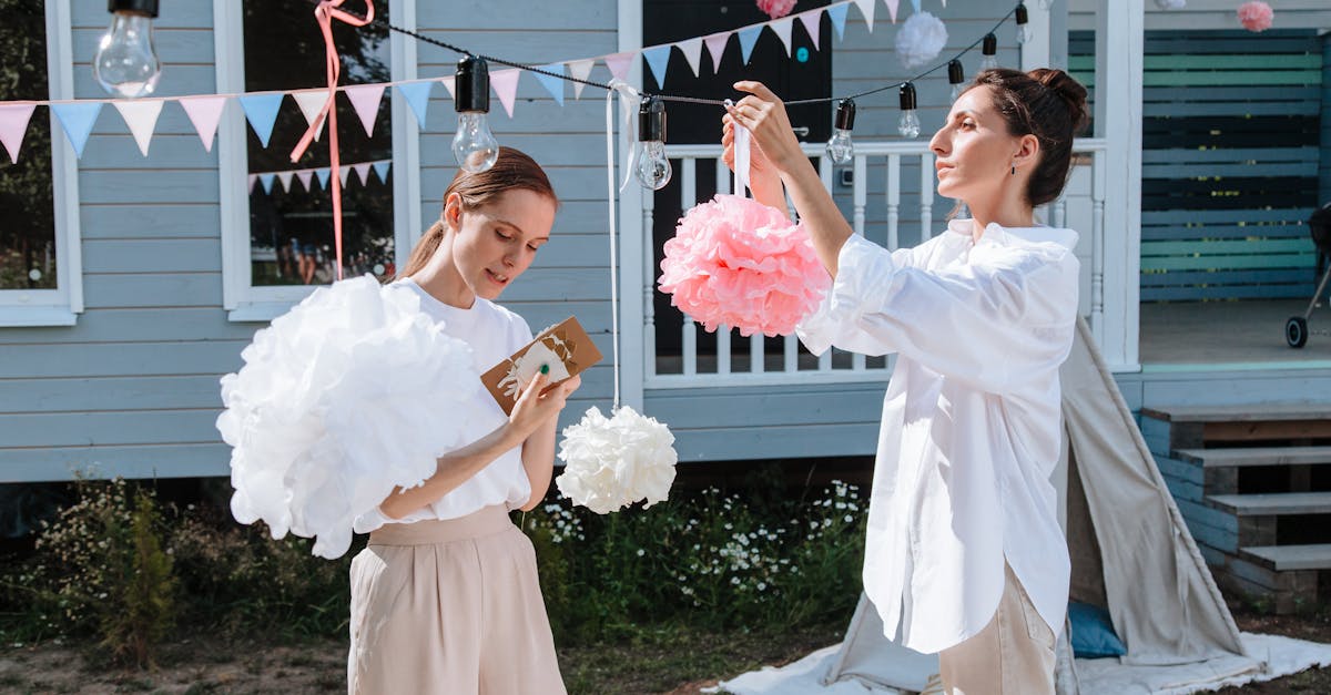 two women in a backyard preparing party decorations with pom poms and lightbulbs