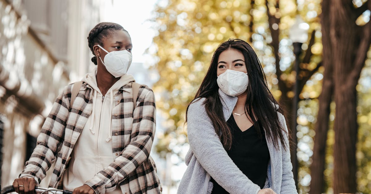 two women wearing masks and holding bicycles enjoying a sunny day outdoors representing friendship