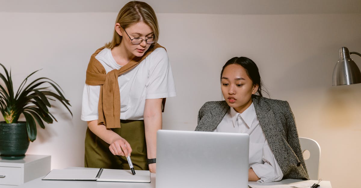 two women working together in a modern office collaborating on a project using a laptop